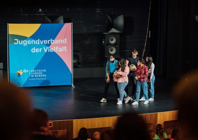 Jugendliche auf der Bühne, Banner mit Aufschrift "Jugendverband der Vielfalt" im Hintergrund