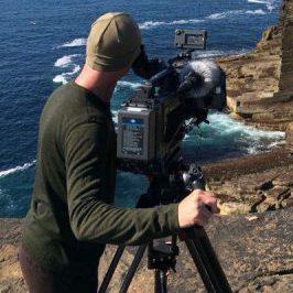 Mensch mit Kamera am Felsen mit Blick auf das Meer im Hintergrund